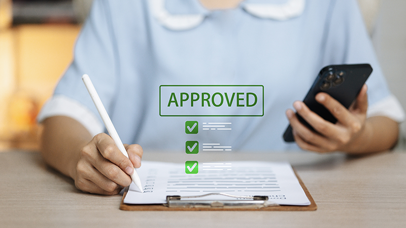 Person holding a phone and pen with 'approved' in green